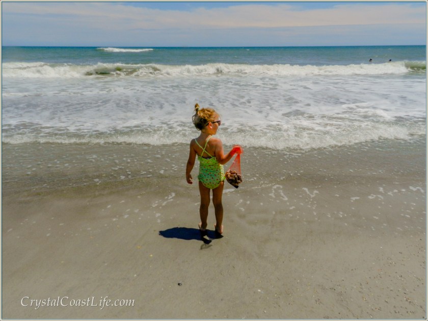 Little girl holding a bag of shells & looking out over the ocean